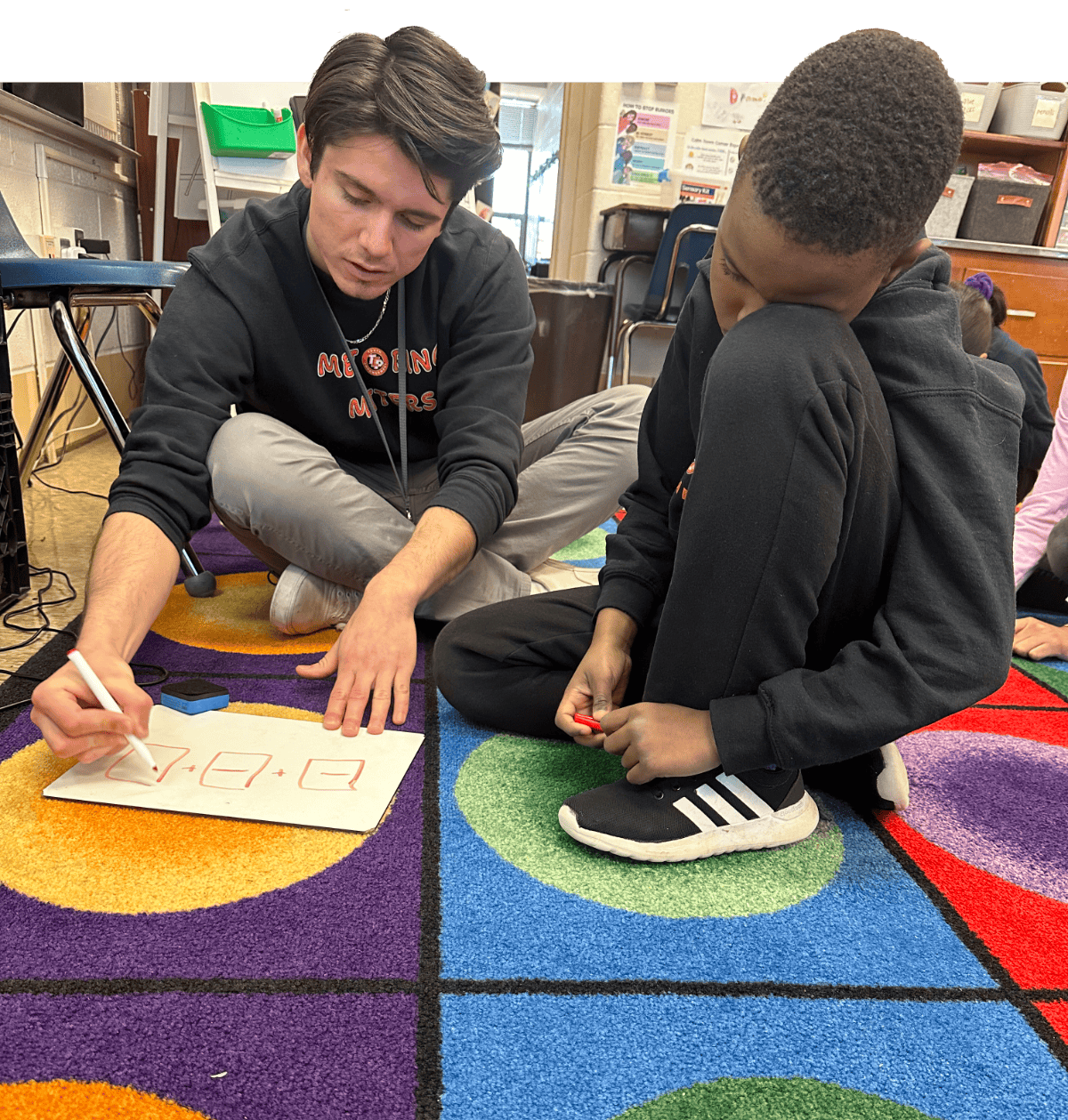 TCP mentor explaining a math problem to a student while hanging out on the floor.